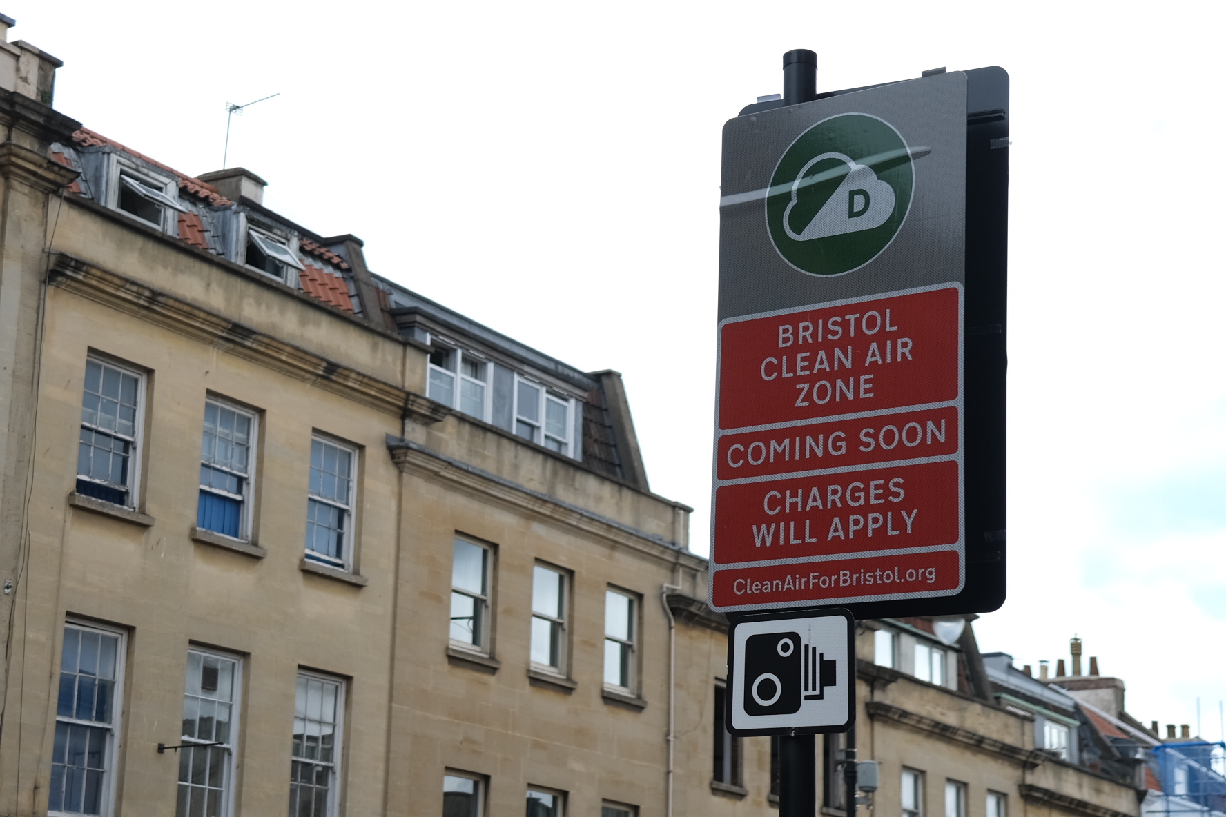 A Bristol Clean Air Zone sign with ‘coming soon’ and ‘charges apply’ written on it, with sky and buildings in the background.