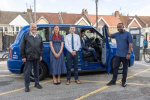 5 people stood by taxi with door open