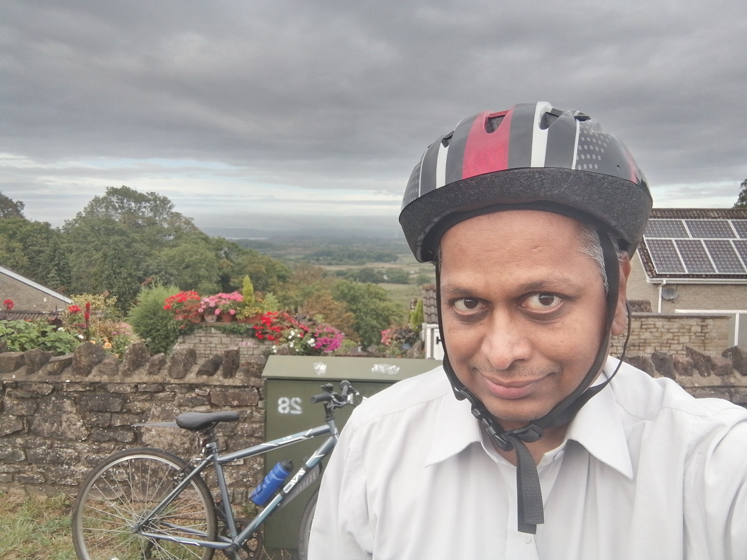 Head and shoulder shot of Mardi Sudhanshu, with countryside and grey skies behind.