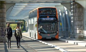 M2 Metro bus on the road with two pedestrians walking on the pavement. 